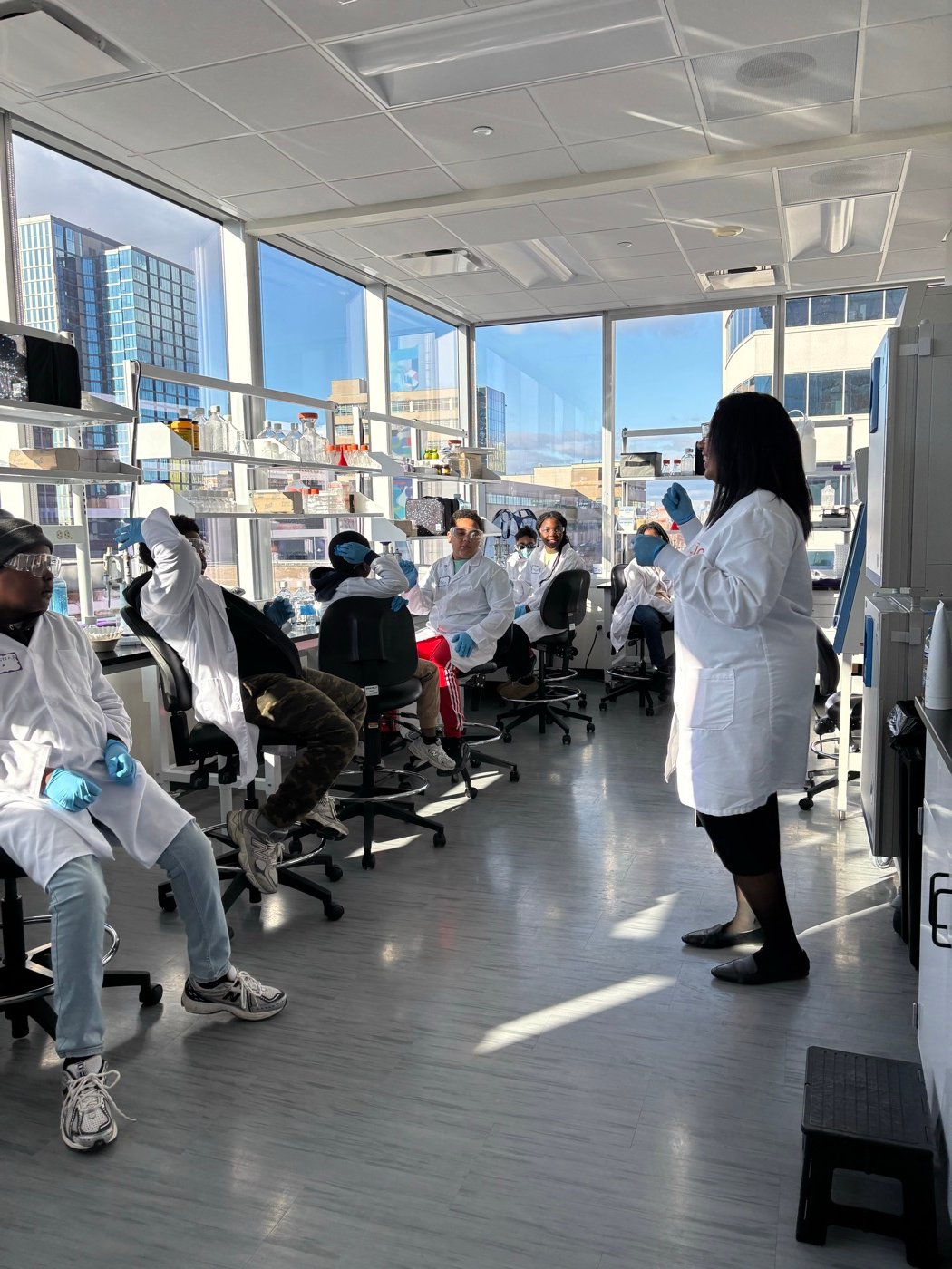 Myettia teaching students in lab coats in a sunlit laboratory